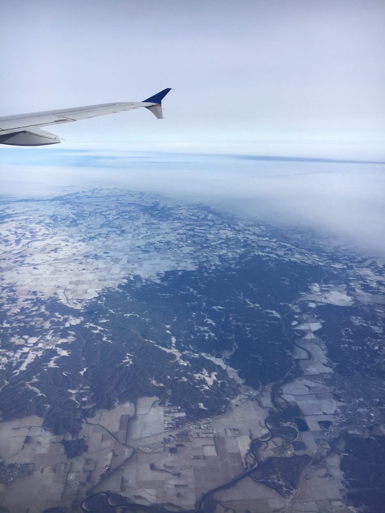 United airplane wing, seen out the window over mountains under cloud cover.